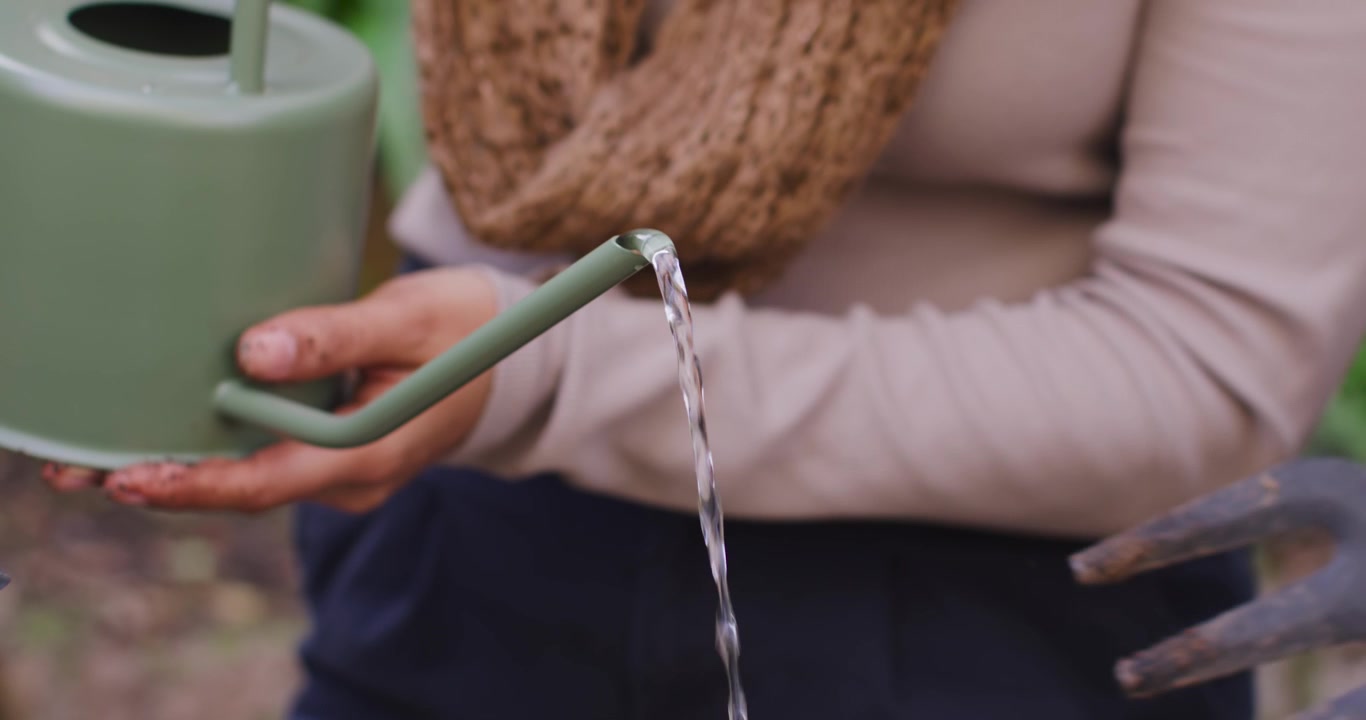 Diverse donne che inclinano un annaffiatoio verde versando acqua su una fioriera sul patio per innaffiare le piantine.