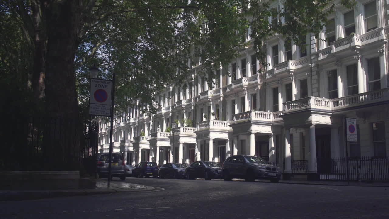 Black cab drives on quiet street in London with white houses neighborhood, Morning Sunlight. Establishing shot