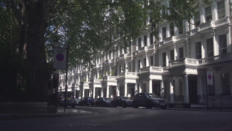 black cab drives on quiet street in london with white houses neighborhood, morning sunlight. establishing shot