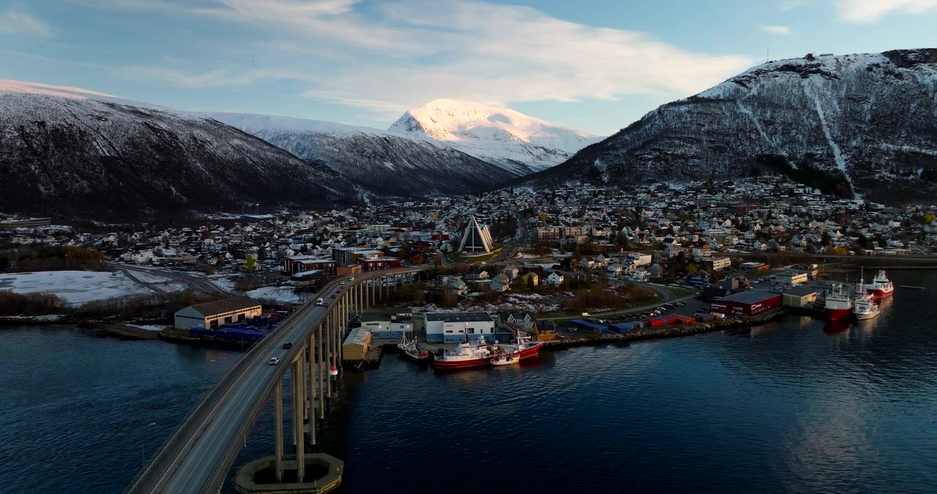 Ville de Tromsø avec sa cathédrale arctique emblématique, adossée à des montagnes hivernales enneigées. Vue par drone.