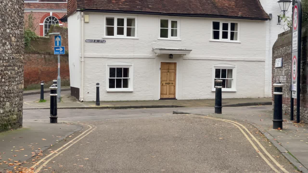 Et statisk bilde viser et sjarmerende hvitt hus med tredør og hvite vinduer, beliggende på et rolig gatehjørne i Winchester, England, med spredte høstblader på fortauet