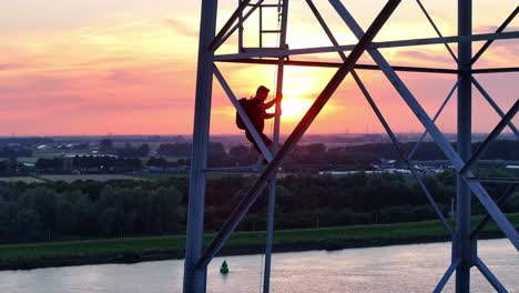 man silhouetted on a high metal tower at sunset