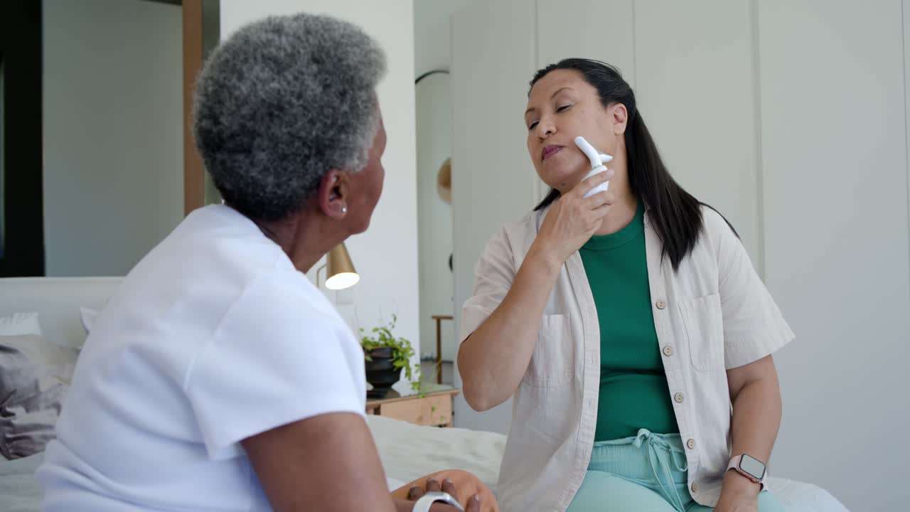 African American daughter picking up groomer on bed, showing jawline motion, teaching senior woman