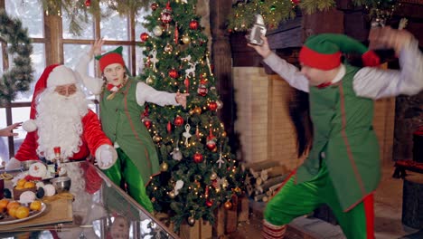 happy elf and santa near the christmas tree. elf is taking photo of a happy fairy characters in decorated room.