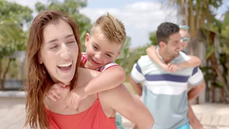 Happy-caucasian-parents-carrying-children-at-swimming-pool-at-beach-house