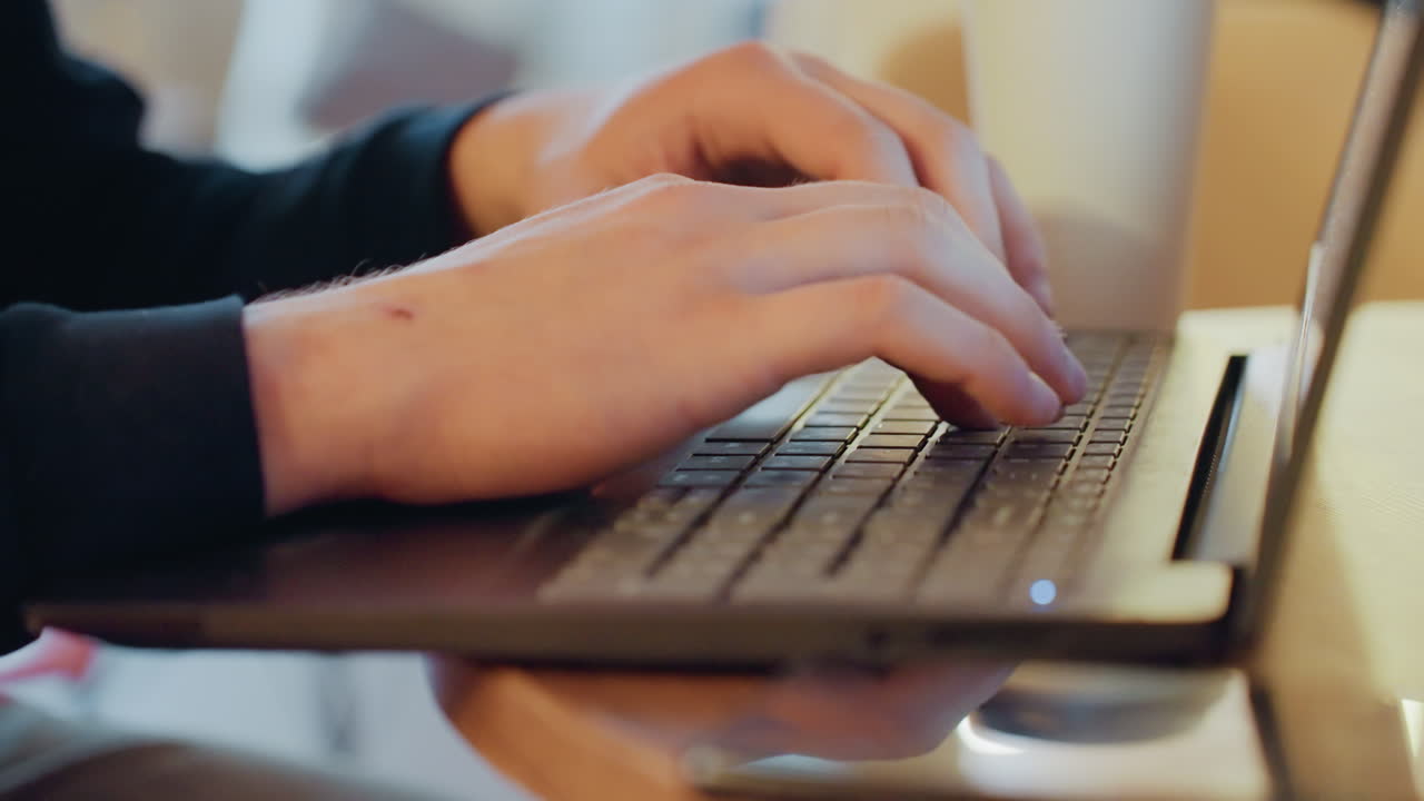 Primo piano di mani che digitano su un laptop, un freelancer in un caffè, luce ambientale calda, tazza di caffè accanto alla tastiera, dita concentrate e battute costanti, maniche di un maglione casual, sfondo bokeh morbido, produttivo