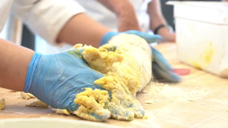 manos humanas con guantes de látex modelando una masa de un tipo típico de pasta italiana hecha con harina, huevos y agua