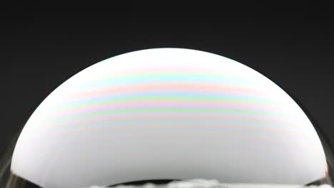a soap bubble expands, displaying vibrant color reflections against a dark background, captured in a smooth, continuous motion