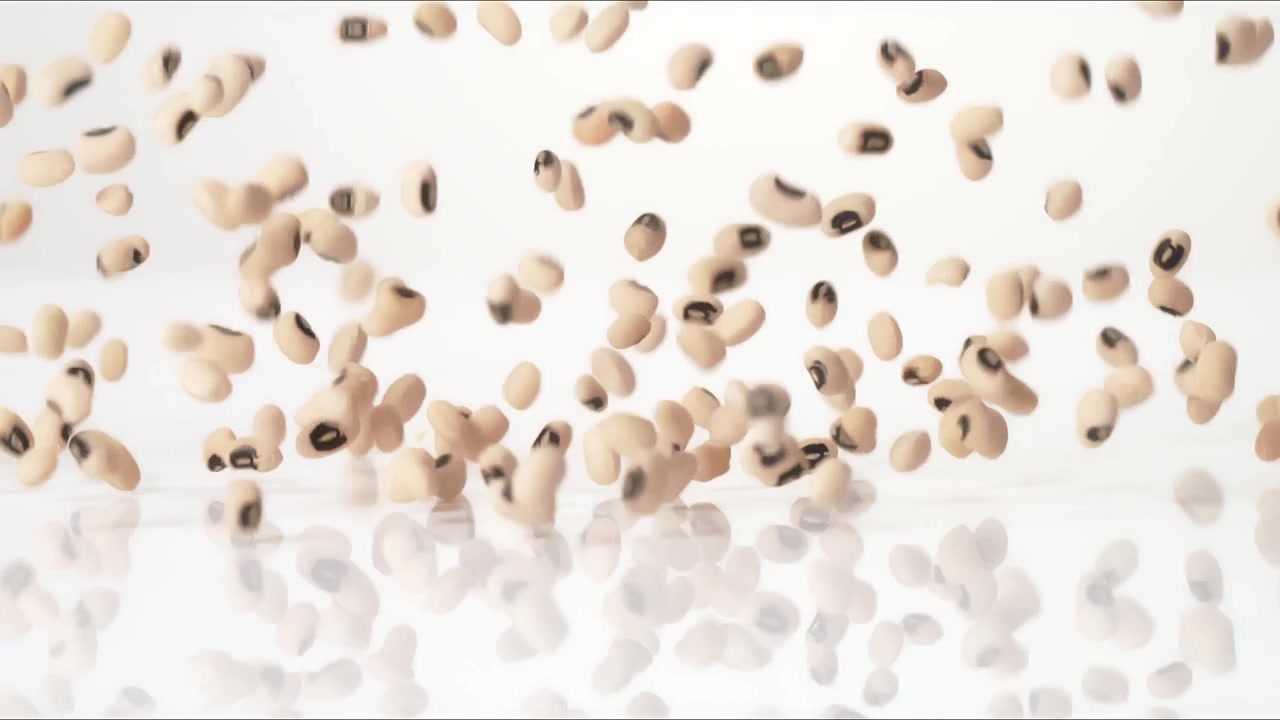 Fagioli dall'occhio nero portafortuna di Capodanno del Sud che rimbalzano su un tavolo bianco al rallentatore, in primo piano macro, prima di posarsi