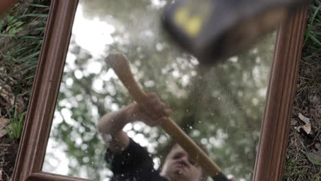 a young high school aged teen boy swings an axe and shatters, breaks a mirror with shards of glass flying