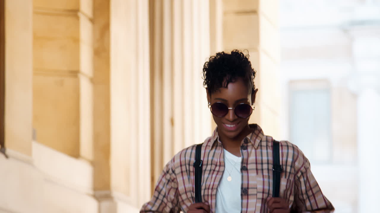 Close up of a fashionable young black woman wearing sunglasses and a plaid shirt walking down stairs outside a historical building, selective focus