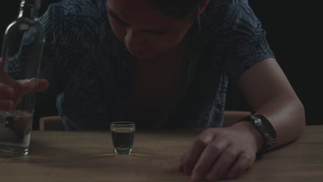 primer plano de un hombre asiático borracho y deprimido vertiendo vodka en un vaso antes de beber y usando un puño rompiendo la mesa en fondo negro