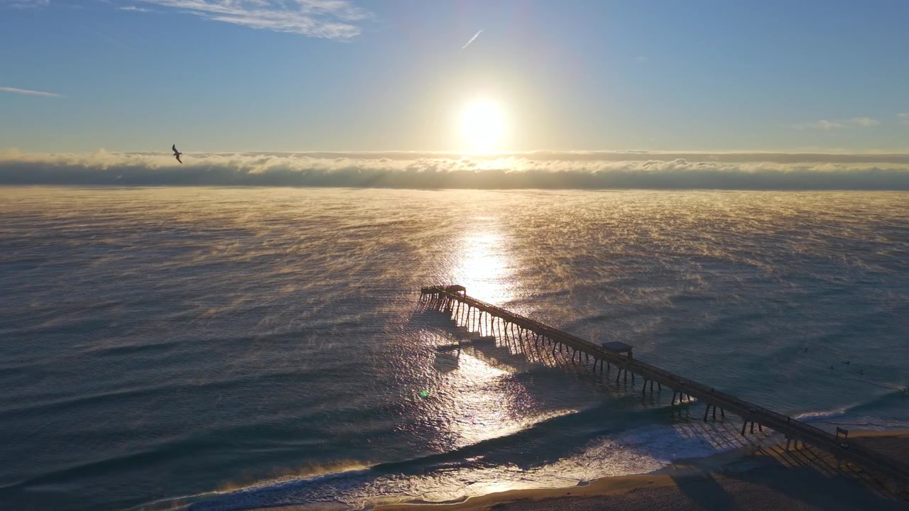 Stationary aerial drone shot above Deerfield Beach at sunrise on a cold morning with steam rising off the ocean and golden morning light