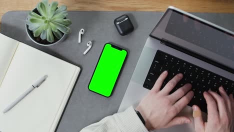 person working at a laptop with green screen phone