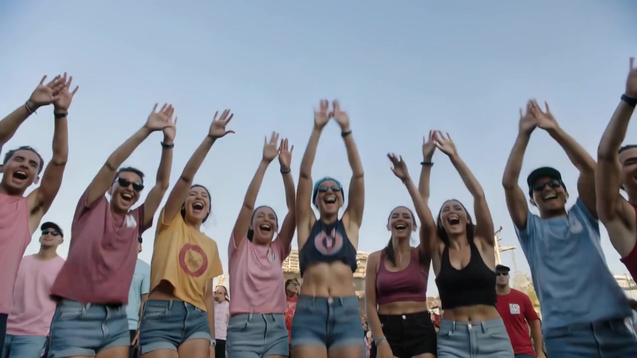 Walking friends approaching camera syncing arms upward, cheering and jumping on grass, denim shorts
