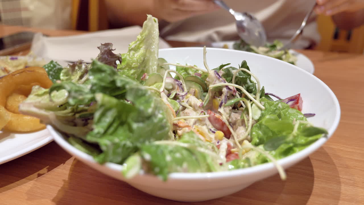 Close-up of an individual mixing a bowl full of vegetable salad with a spoon and a fork at a restaurant in Bangkok, Thailand
