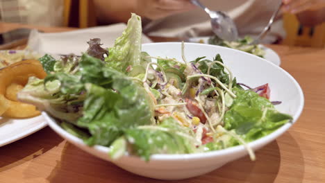 primer plano de un individuo mezclando un cuenco lleno de ensalada de verduras con una cuchara y un tenedor en un restaurante en bangkok, tailandia