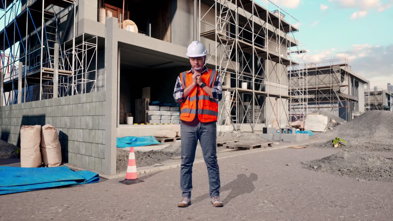 Full Body Of Asian Male Engineer With Safety Helmet Pray For Something While Standing At Building & Construction Site in Progress to New House