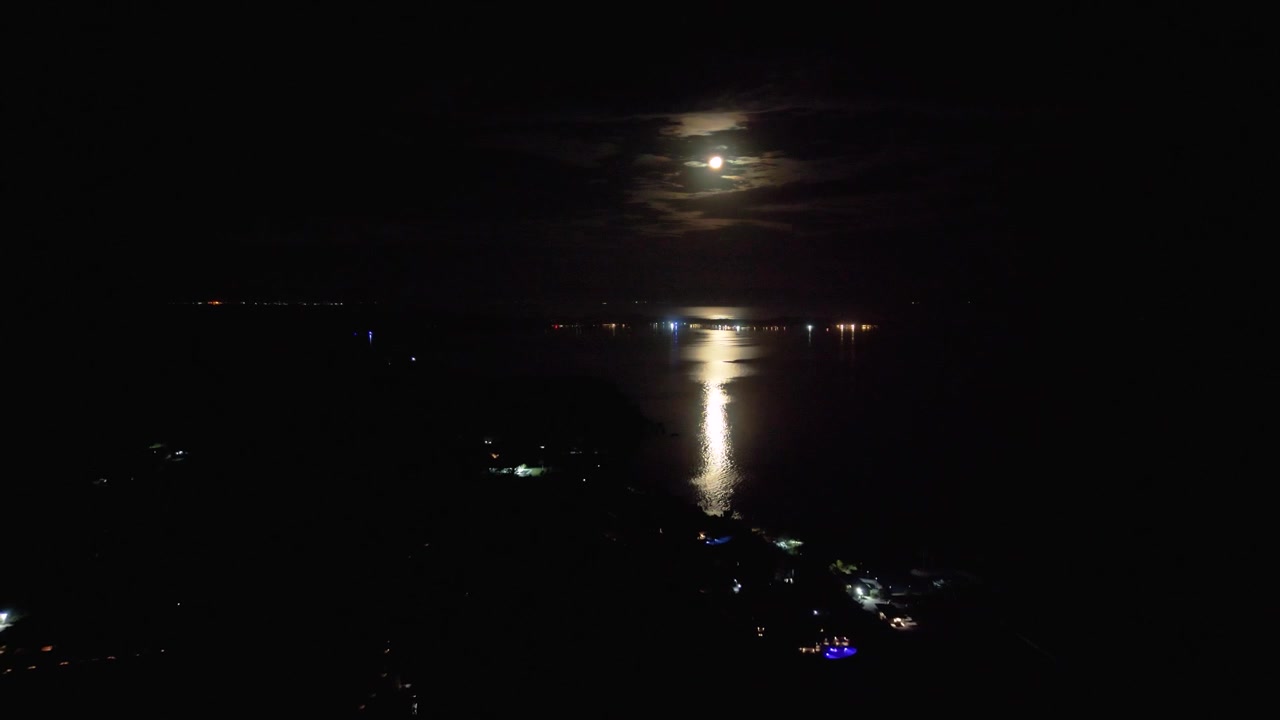 Luna piena che splende attraverso le nuvole e si riflette sull'Oceano Pacifico calmo durante una notte tranquilla sull'isola di Malolo, Fiji.