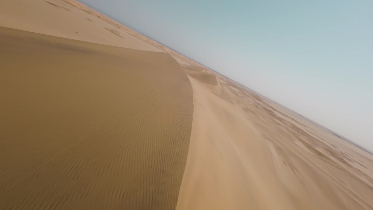 Filmato dinamico con drone FPV che orbita e si muove intorno a dune di sabbia nel deserto della Namibia da un'angolazione diversa, mostrando un vasto paesaggio arido e forme di dune spettacolari.