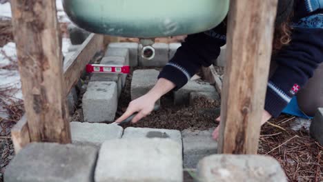 the man is compressing the concrete block and then employing a level to align it beneath the diy hot tub - close up