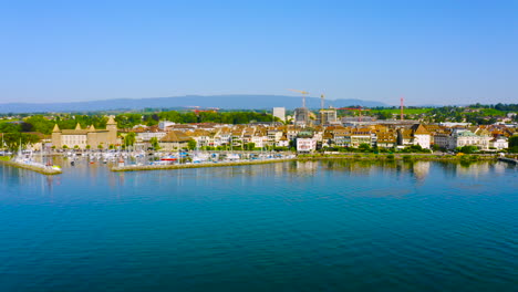 calm water of lake leman with morges town and castle on the background at daytime in vaud, switzerland - aerial drone - low panning shot