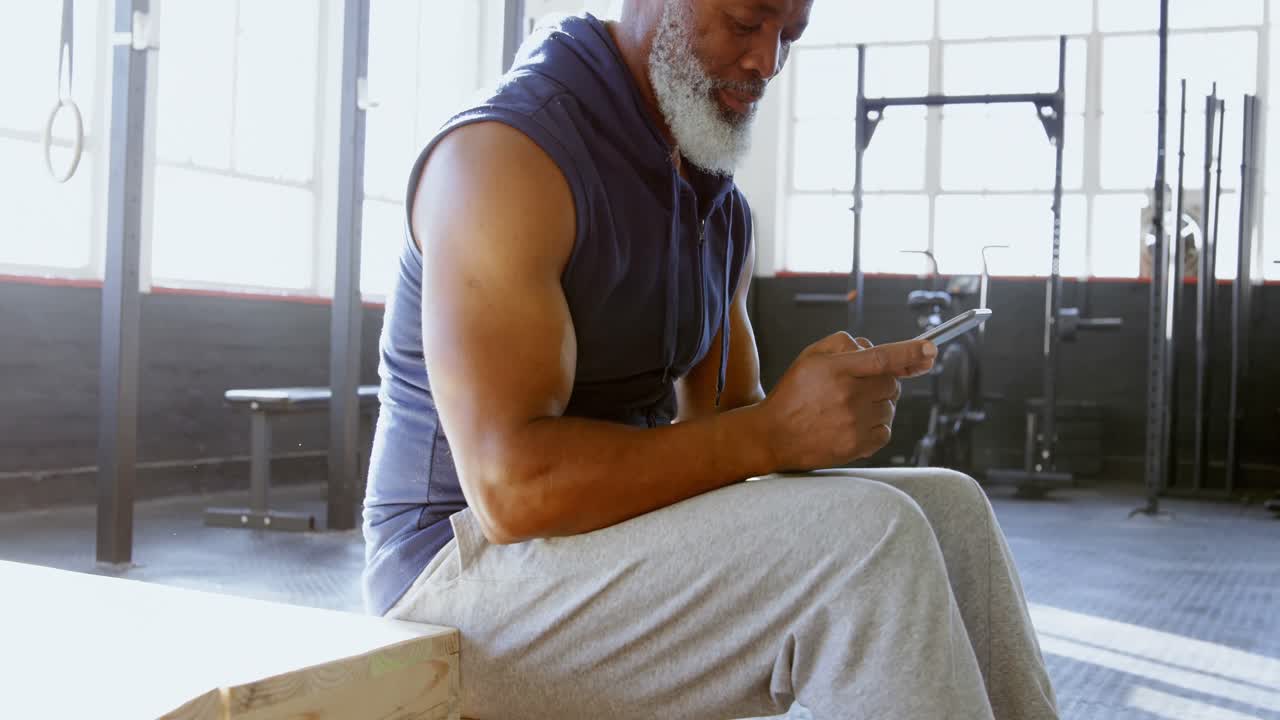 hombre mayor usando un teléfono inteligente en un gimnasio 4k