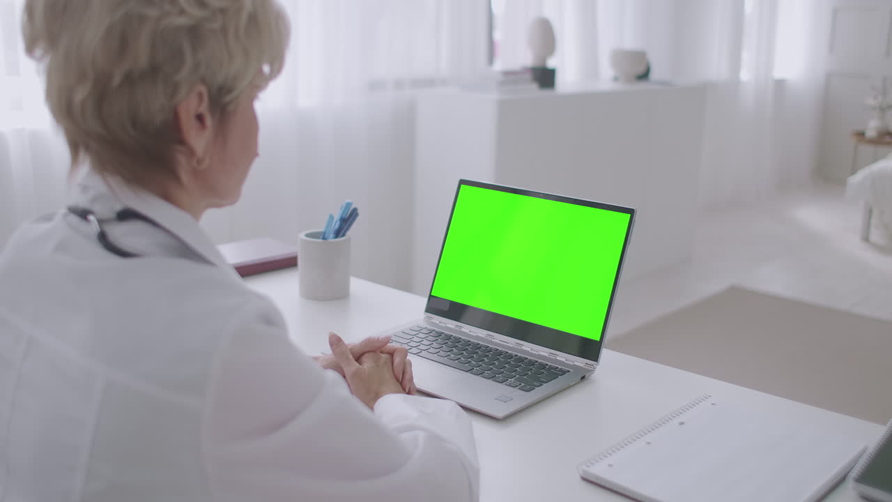 una anciana médica está trabajando de forma remota consulta en línea mirando la pantalla verde de la computadora portátil para la tecnología de clave de croma telemedicina