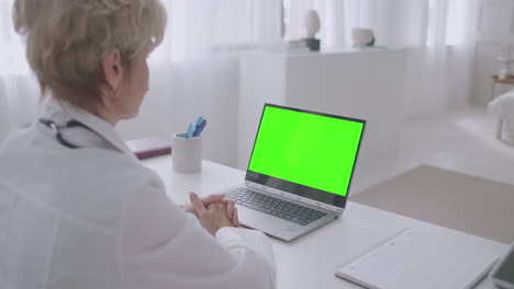aged-female-doctor-is-working-remotely-online-consultation-looking-at-green-screen-of-laptop-for-chroma-key-technology-telemedicine