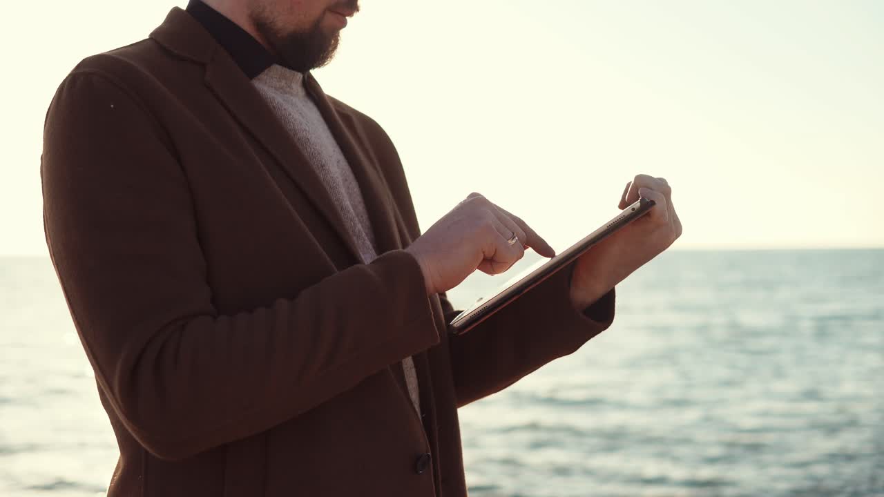해가 지는 해변에서 태블릿을 사용하는 남자