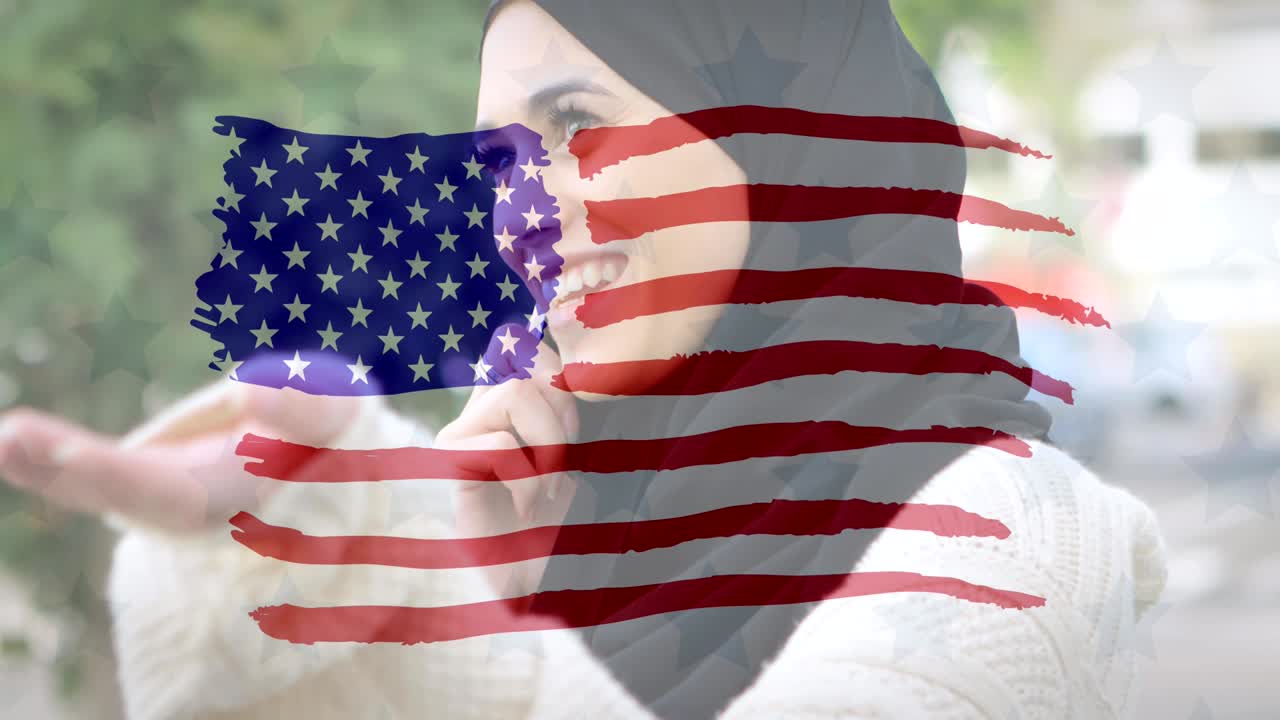 Animation of American flag drawn over mixed race woman in hijab talking on her smartphone