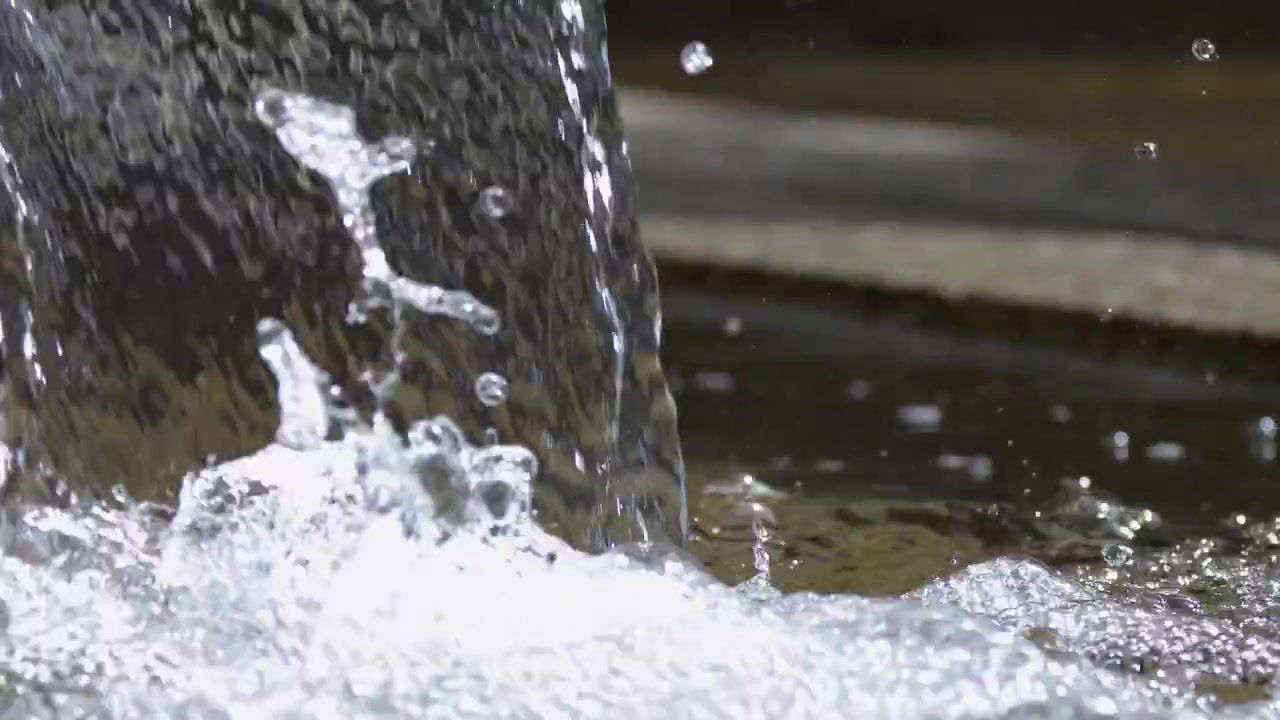 明るい日中の光の中、石の鉢に水が流れ込み、跳ねる様子を捉えた静止したクローズアップショット。