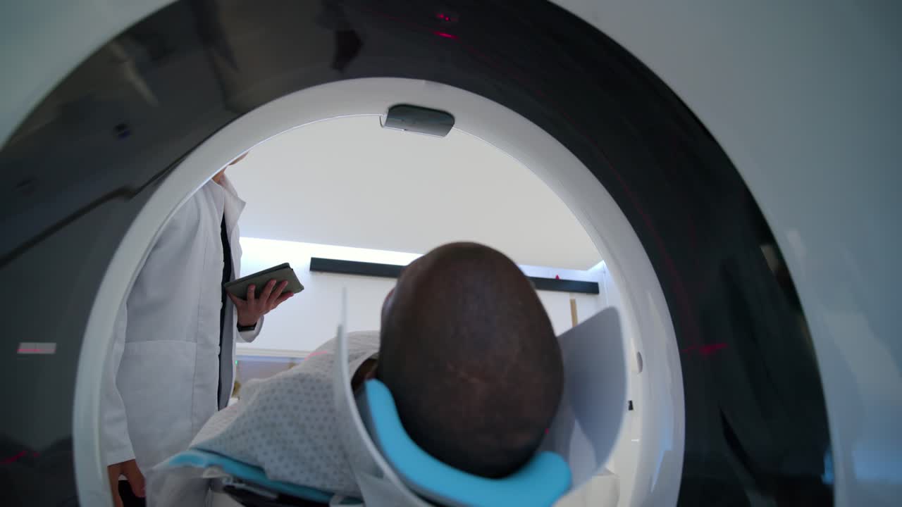 Il tecnico sta modificando la bobina della testa mentre il medico spiega la procedura e prepara il paziente per l'imaging