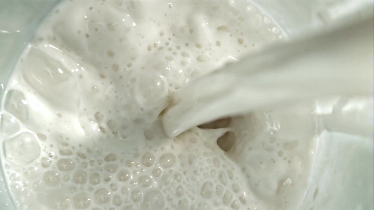 Primo piano di latte fresco e bianco che viene versato e schizza in un contenitore.