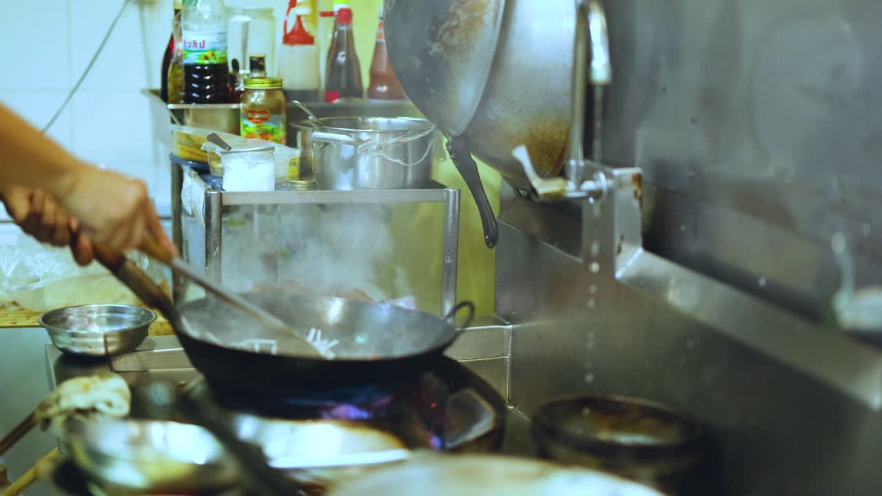 Chef stir-frying noodles in a hot wok