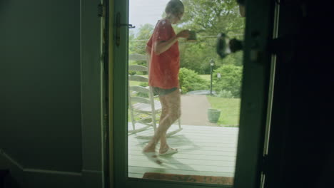 young woman walking out her front door to sit on a rocking chair and sip tea on her front porch