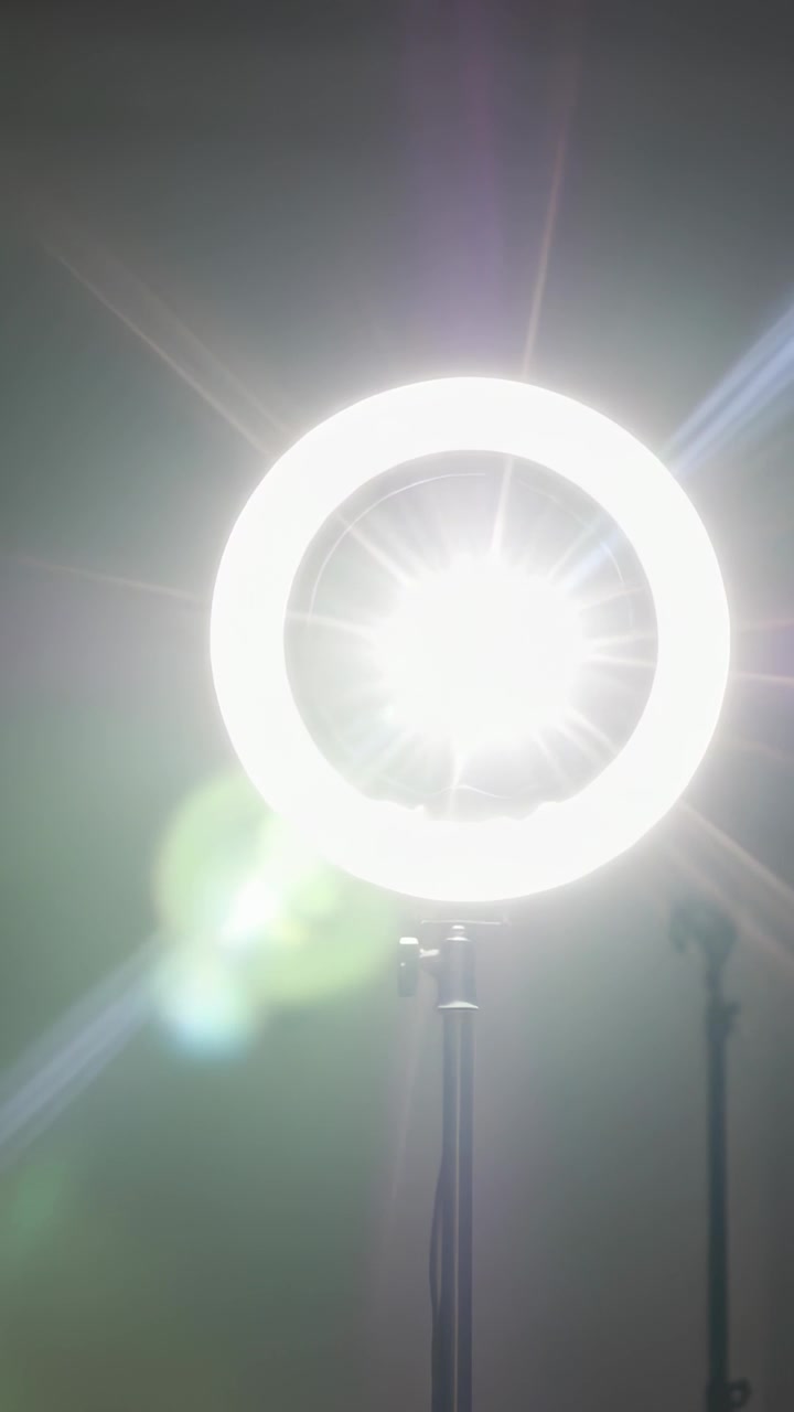 Vídeo vertical: Ligando luz de anel LED deslizando no centro do teto, tripé, reflexos de lente iluminando estúdio
