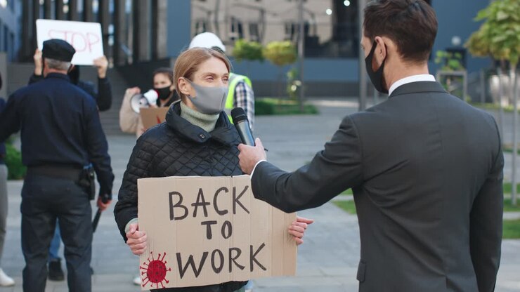 Rear view of a caucasian journalist or correspondent in a interview with a caucasian woman who is wearing protective mask in a protest against Covid 19