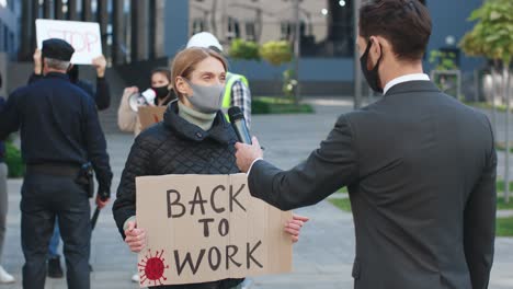 rear view of a caucasian journalist or correspondent in a interview with a caucasian woman who is wearing protective mask in a protest against covid 19