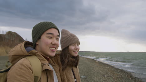 close up view of two teenage in winter clothes on seashore talking and looking the ocean on a windy day