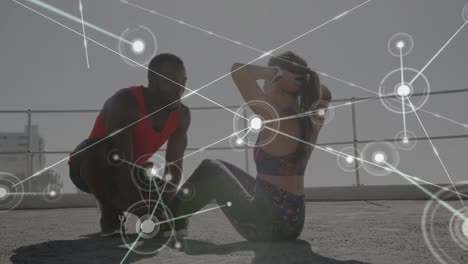 Network-of-connections-against-mixed-race-couple-performing-abs-exercise-together-on-the-promenade