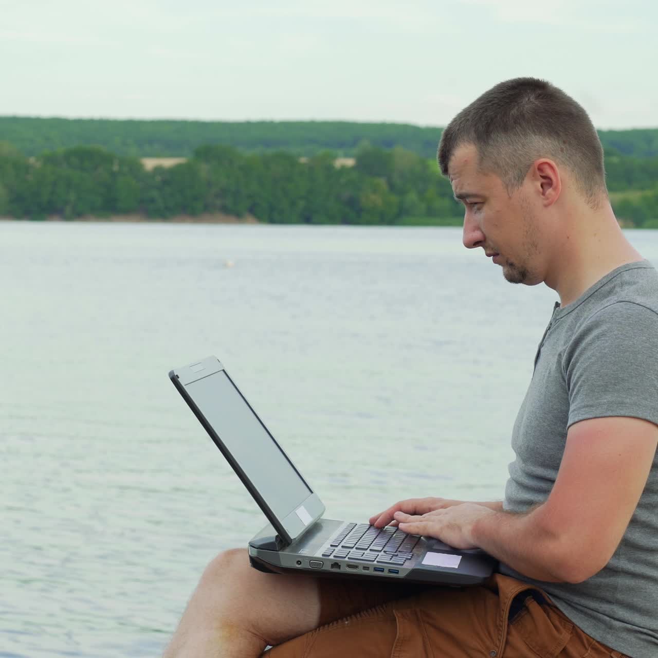 Handsome man sitting on a wooden pier with laptop