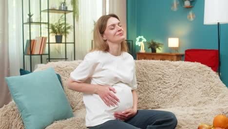 pregnant woman holds belly breathes during mild contractions smiles listens to baby movement on sofa