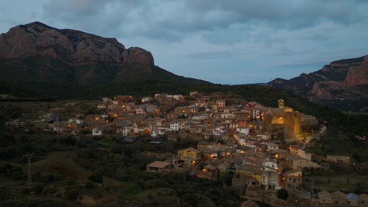 Borgo medievale in pietra al crepuscolo con chiesa illuminata e montagna