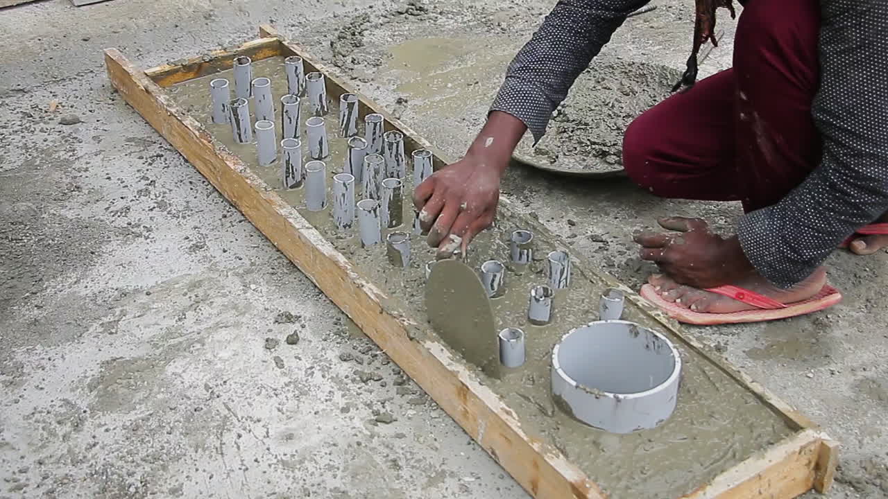 Indian mason worker placing wet concrete mix into a slab around pipes, leveling with trowel for smoothness
