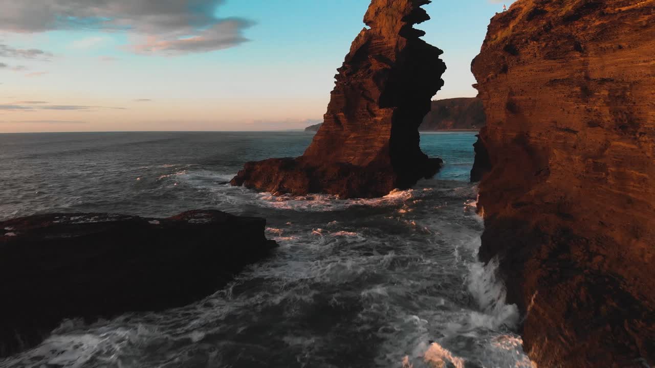 los acantilados de la playa de piha se pintan de colores cálidos a la hora dorada