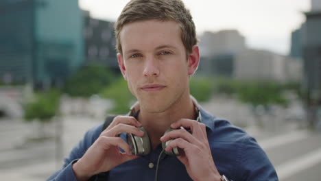 retrato en primer plano de un atractivo hombre caucásico estudiante escuchando música quita los auriculares sonriendo con confianza a la cámara en el fondo de la ciudad