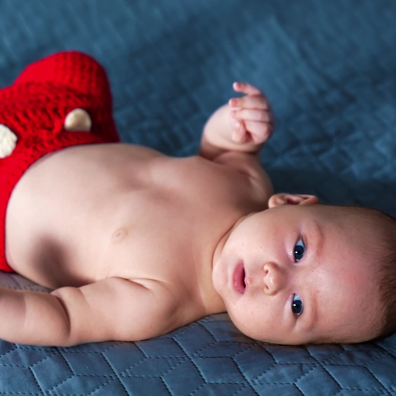 Baby boy lying on face up in red pants with white buttons and socks. Lovely infant kid staying calm and peaceful. Close up
