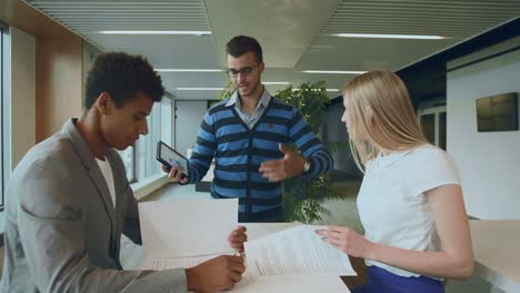 multiethnic coworkers with papers and tablet. side view of black man with coworkers at table reading papers and using tablet in team at table