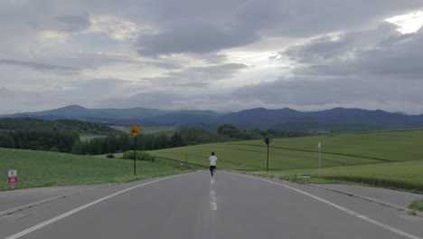 man running straight on white stripe of empty countryside asphalted road, rear view